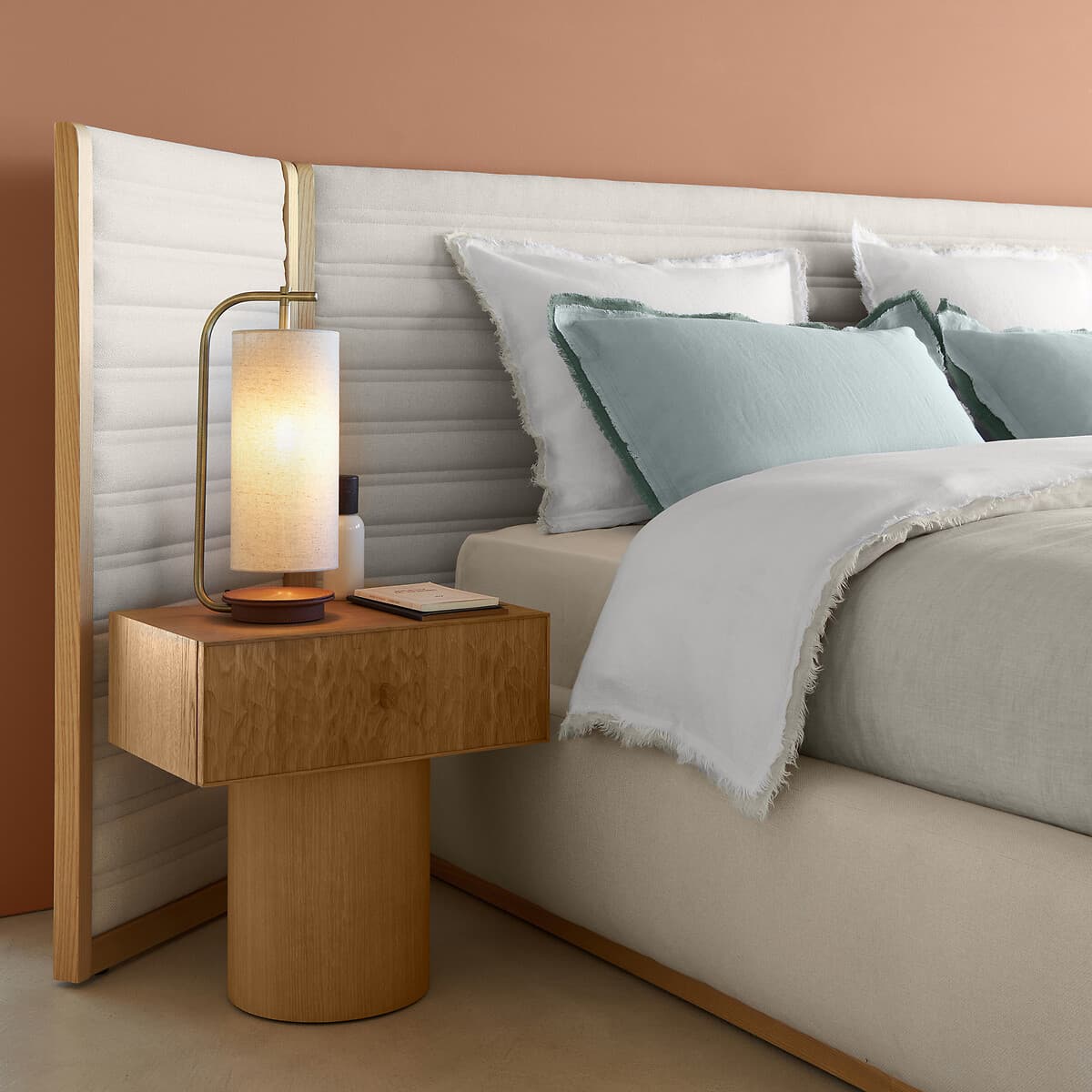 Mesita de noche de madera clara con lámpara dorada